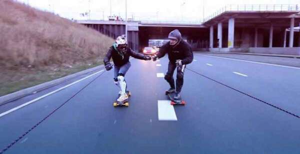 Two guys on skateboards at an Amsterdam Highway, town by a Opel Adam car