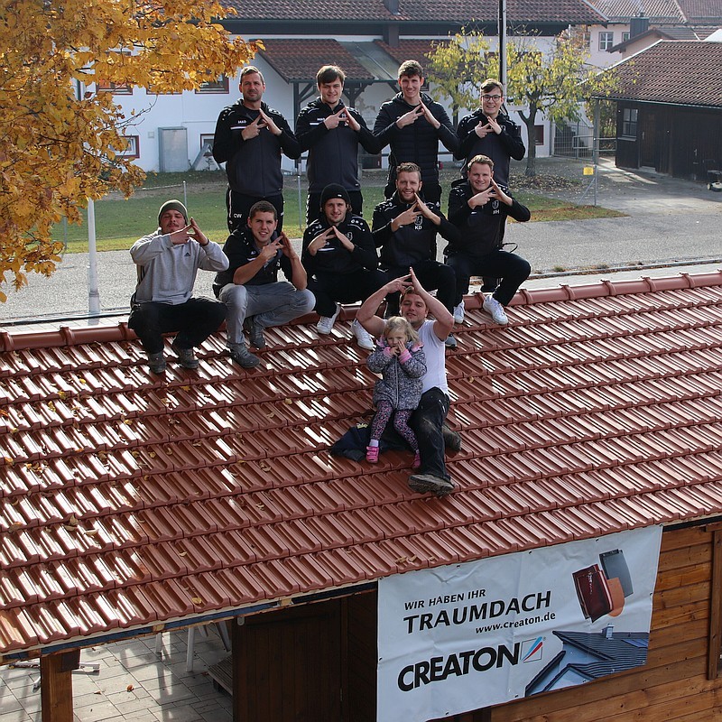 10 Zimmerei Mitarbeiter mit Meister und Kind auf dem fertigen Dach, alle machen den Geste #Dachdrauf