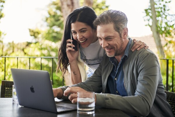 couple smiling while engaging with laptop and smartphone